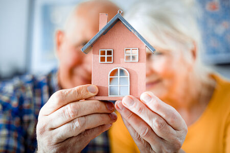 Senior couple holding a small model of a house in the foreground of the image