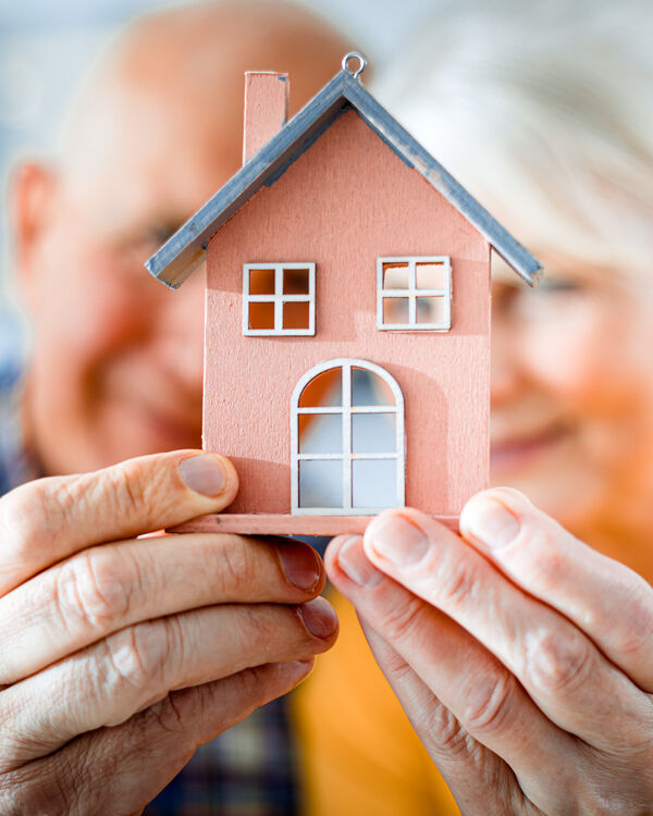 Senior couple holding a small model of a house in the foreground of the image